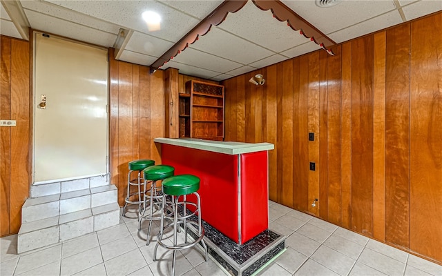 bar featuring wooden walls, light tile patterned floors, and a paneled ceiling