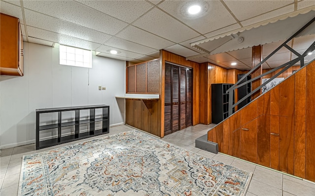 basement with wood walls, a paneled ceiling, and light tile patterned floors