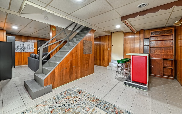 basement featuring bar area, wood walls, light tile patterned floors, and a paneled ceiling