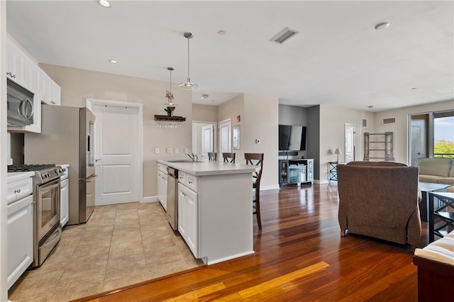 kitchen featuring appliances with stainless steel finishes, hanging light fixtures, white cabinets, light wood-type flooring, and sink