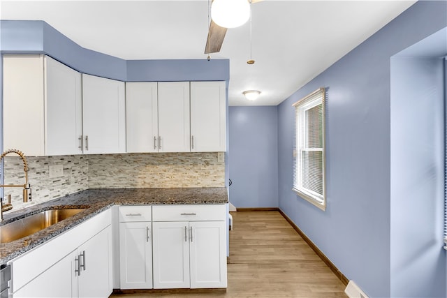 kitchen featuring light hardwood / wood-style floors, sink, white cabinetry, decorative backsplash, and dark stone countertops