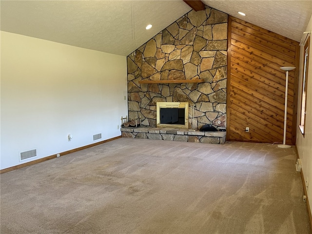 unfurnished living room featuring a textured ceiling, lofted ceiling with beams, a stone fireplace, and carpet floors