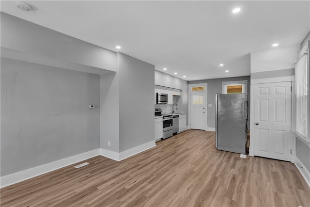 kitchen featuring white cabinets, sink, stainless steel appliances, light wood-type flooring, and decorative backsplash