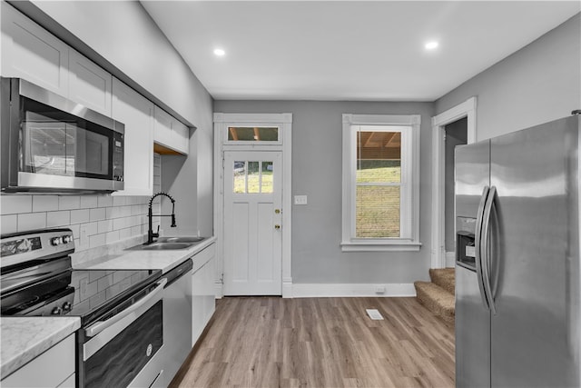 kitchen with sink, white cabinets, light hardwood / wood-style flooring, backsplash, and appliances with stainless steel finishes