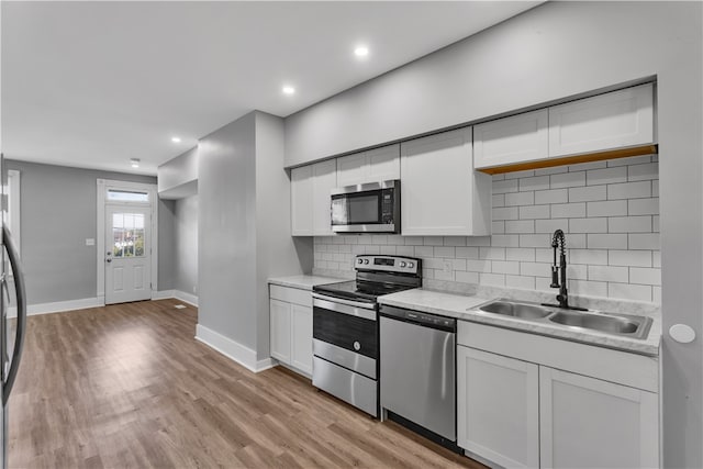 kitchen with appliances with stainless steel finishes, light wood-type flooring, white cabinetry, and sink