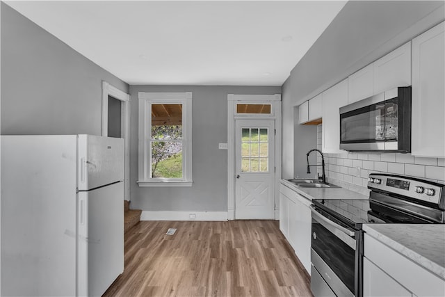 kitchen with light hardwood / wood-style floors, sink, white cabinets, backsplash, and appliances with stainless steel finishes