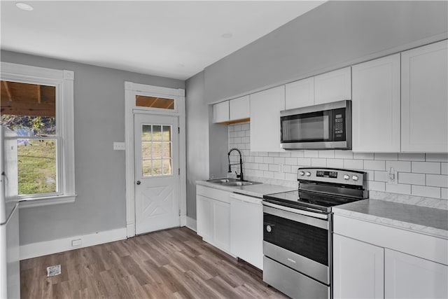 kitchen with appliances with stainless steel finishes, white cabinetry, sink, and light hardwood / wood-style flooring