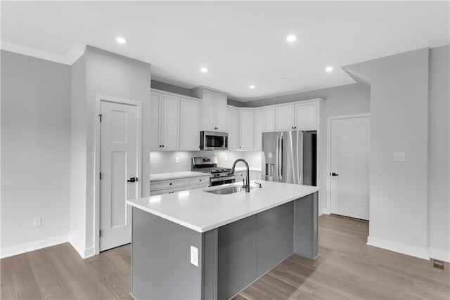 kitchen with appliances with stainless steel finishes, an island with sink, white cabinets, light hardwood / wood-style flooring, and sink