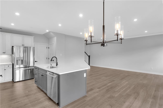 kitchen with an island with sink, hanging light fixtures, light hardwood / wood-style flooring, appliances with stainless steel finishes, and an inviting chandelier