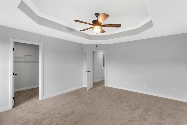 unfurnished bedroom featuring ceiling fan, a raised ceiling, a walk in closet, a closet, and light colored carpet