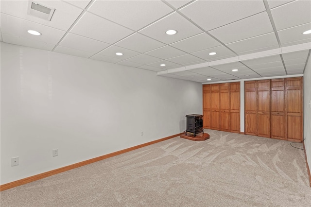 basement with a drop ceiling, a wood stove, and carpet