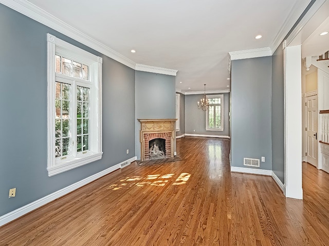 unfurnished living room featuring a notable chandelier, hardwood / wood-style flooring, ornamental molding, and a brick fireplace