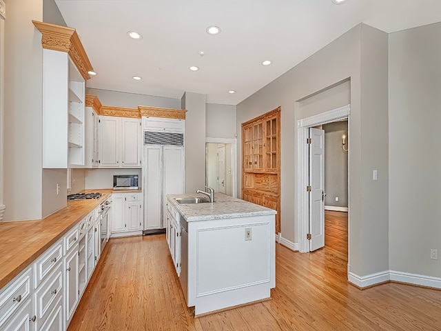 kitchen with white cabinets, an island with sink, sink, stainless steel appliances, and light wood-type flooring