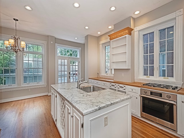 kitchen with light hardwood / wood-style floors, white cabinets, stainless steel appliances, a center island with sink, and sink