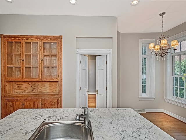 kitchen featuring light stone counters, pendant lighting, wood-type flooring, sink, and a notable chandelier