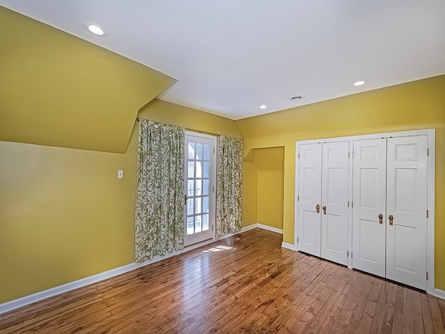 unfurnished bedroom featuring vaulted ceiling, a closet, and hardwood / wood-style flooring