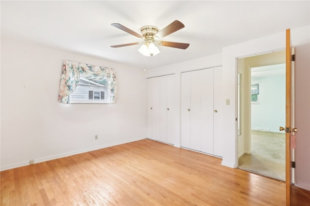 unfurnished bedroom featuring multiple closets, ceiling fan, and hardwood / wood-style flooring