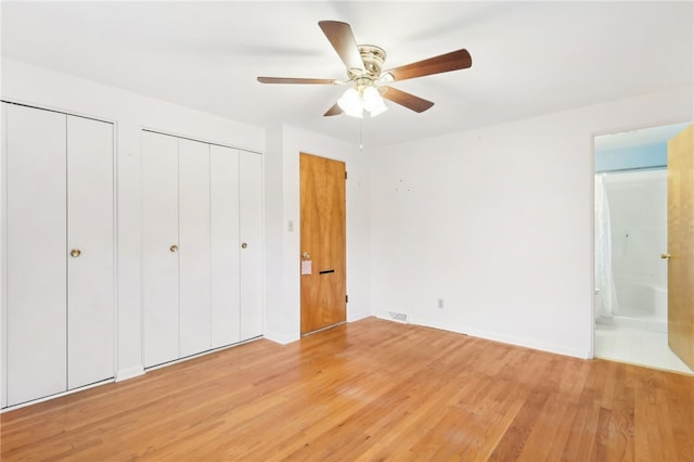 unfurnished bedroom featuring ceiling fan, multiple closets, ensuite bath, and hardwood / wood-style floors