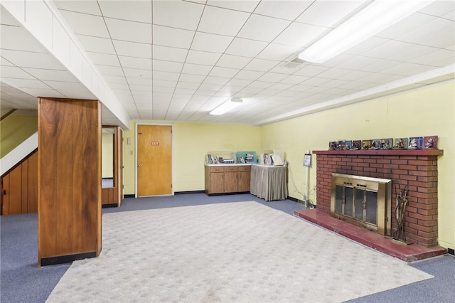 carpeted living room featuring a brick fireplace and a drop ceiling