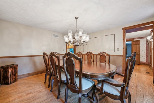 dining space featuring an inviting chandelier, light hardwood / wood-style floors, and a textured ceiling