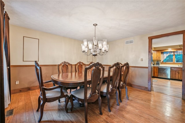 dining area with a textured ceiling, light wood-type flooring, and a chandelier