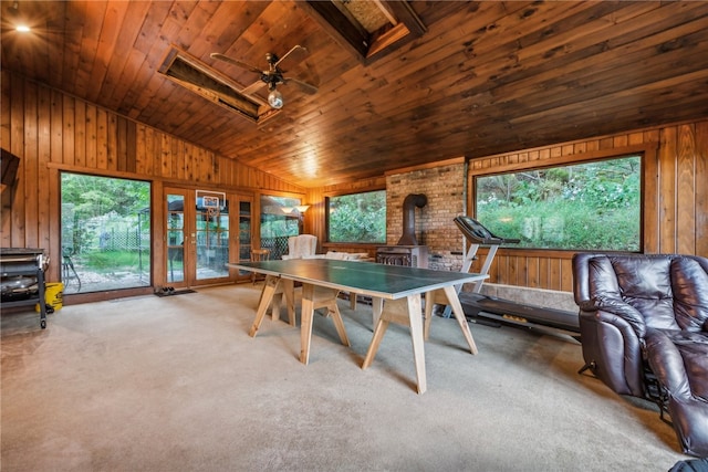 interior space with ceiling fan, wood ceiling, a wood stove, wooden walls, and carpet floors