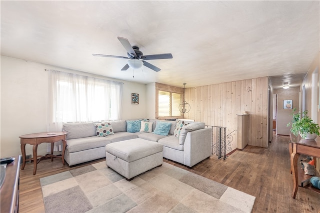 living room with ceiling fan, light wood-type flooring, and wood walls