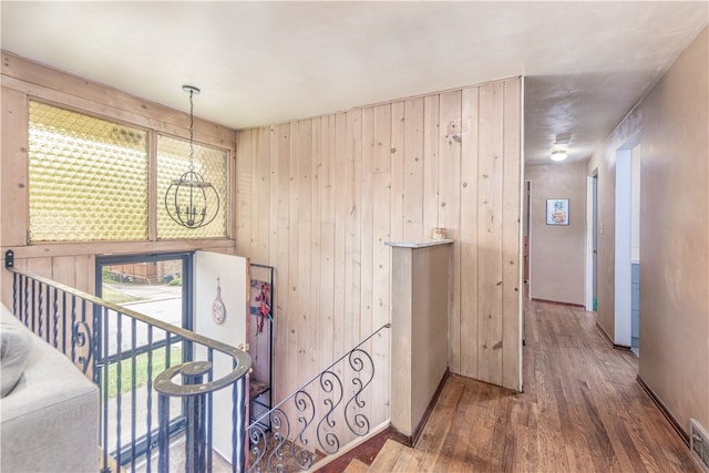 hallway with an inviting chandelier, wood walls, and hardwood / wood-style floors