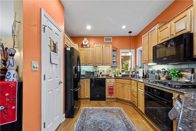 kitchen featuring decorative backsplash, light wood-type flooring, black appliances, decorative light fixtures, and dark stone counters