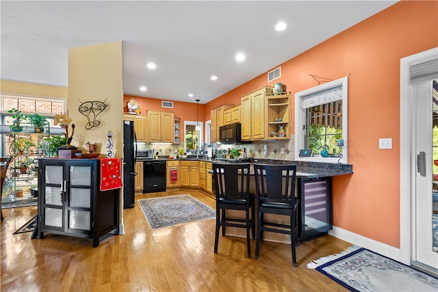 kitchen with kitchen peninsula, black appliances, light wood-type flooring, a kitchen bar, and decorative backsplash