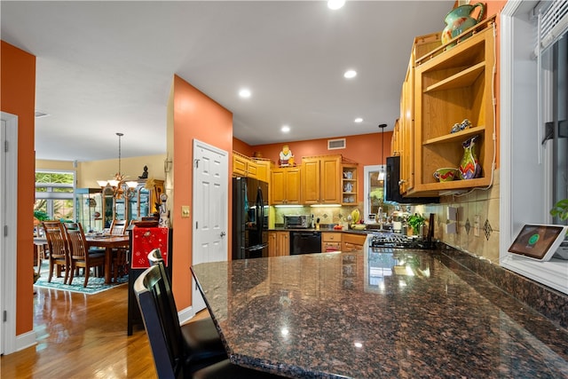 kitchen featuring kitchen peninsula, wood-type flooring, decorative light fixtures, black appliances, and a breakfast bar area