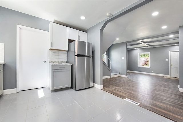 kitchen featuring light wood-type flooring, beamed ceiling, white cabinetry, light stone countertops, and stainless steel fridge