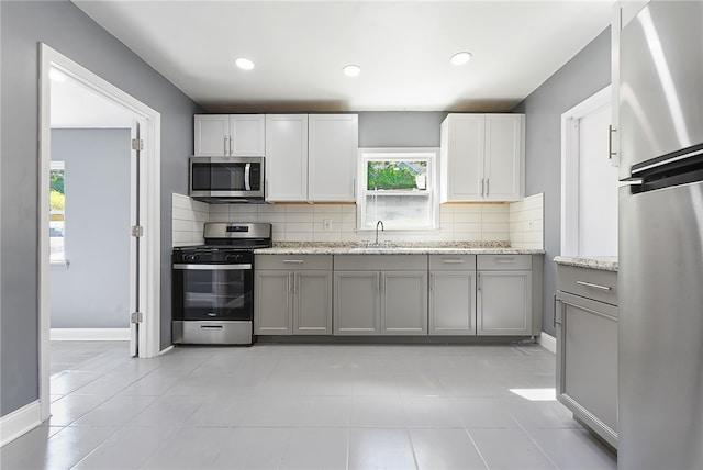 kitchen featuring appliances with stainless steel finishes, a healthy amount of sunlight, gray cabinetry, and light stone counters