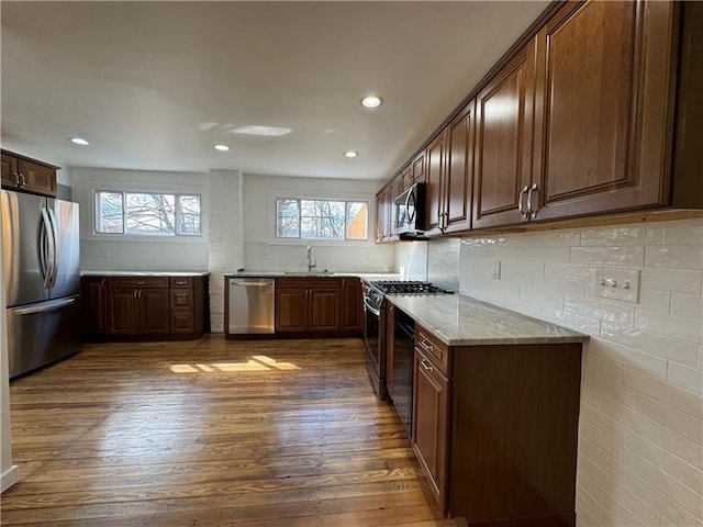 kitchen with dark brown cabinets, light stone counters, dark hardwood / wood-style floors, sink, and stainless steel appliances