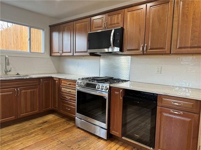 kitchen with appliances with stainless steel finishes, decorative backsplash, light stone counters, light hardwood / wood-style flooring, and sink