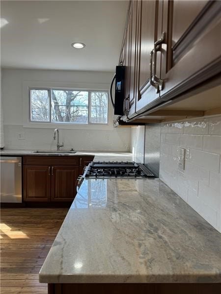 kitchen with light stone counters, sink, tasteful backsplash, stainless steel dishwasher, and dark wood-type flooring