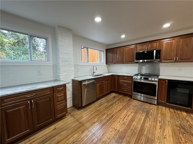 kitchen featuring appliances with stainless steel finishes, tasteful backsplash, light stone countertops, light wood-type flooring, and sink