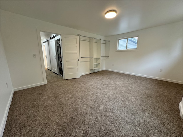 unfurnished bedroom featuring dark colored carpet and a barn door