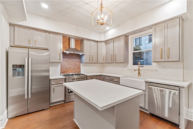 kitchen featuring an inviting chandelier, light wood-type flooring, appliances with stainless steel finishes, and wall chimney range hood