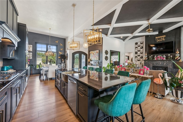 kitchen with light wood-type flooring, a kitchen island with sink, a breakfast bar area, beam ceiling, and hanging light fixtures