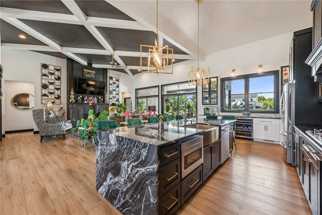 kitchen featuring an island with sink, sink, beverage cooler, dark stone counters, and light wood-type flooring