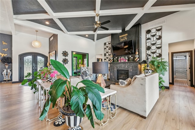 living room featuring coffered ceiling, beam ceiling, ceiling fan, light hardwood / wood-style flooring, and french doors