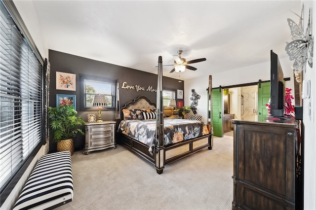 bedroom featuring light carpet, ensuite bath, ceiling fan, and a barn door