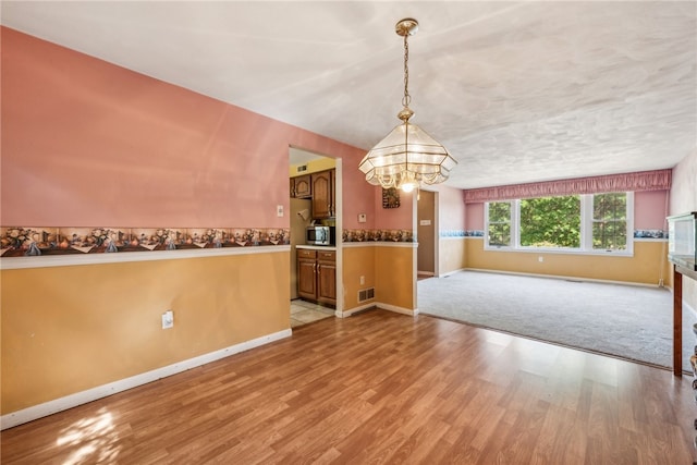 unfurnished dining area featuring an inviting chandelier and light hardwood / wood-style floors