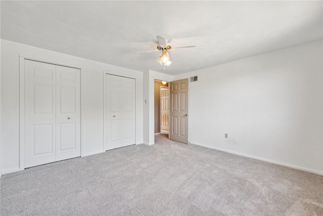 unfurnished bedroom with light carpet, two closets, and ceiling fan