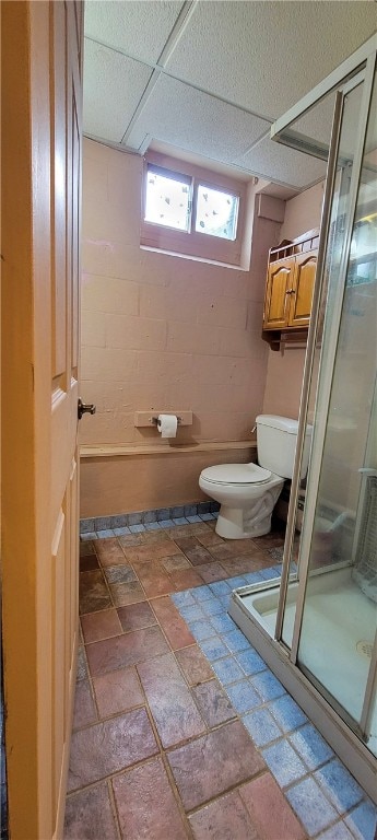 bathroom with a drop ceiling, toilet, and a shower with shower door