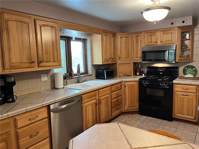 kitchen with appliances with stainless steel finishes, tile counters, backsplash, and sink