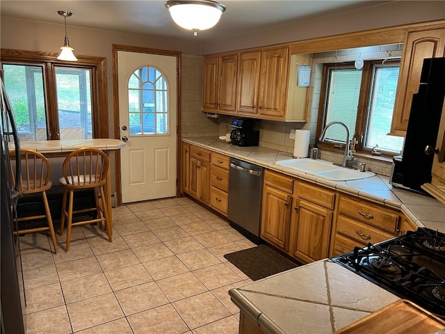 kitchen with pendant lighting, tasteful backsplash, sink, tile countertops, and stainless steel dishwasher