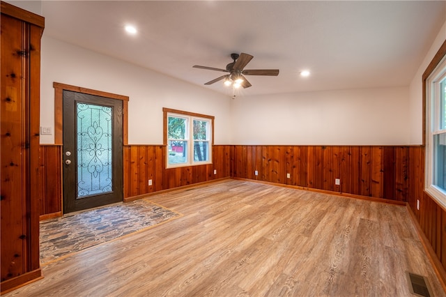 unfurnished room with light wood-type flooring, wood walls, and ceiling fan