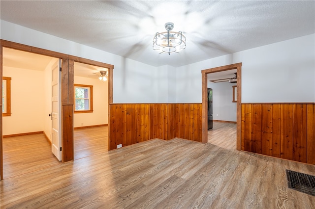 empty room featuring light hardwood / wood-style flooring, a textured ceiling, and ceiling fan with notable chandelier